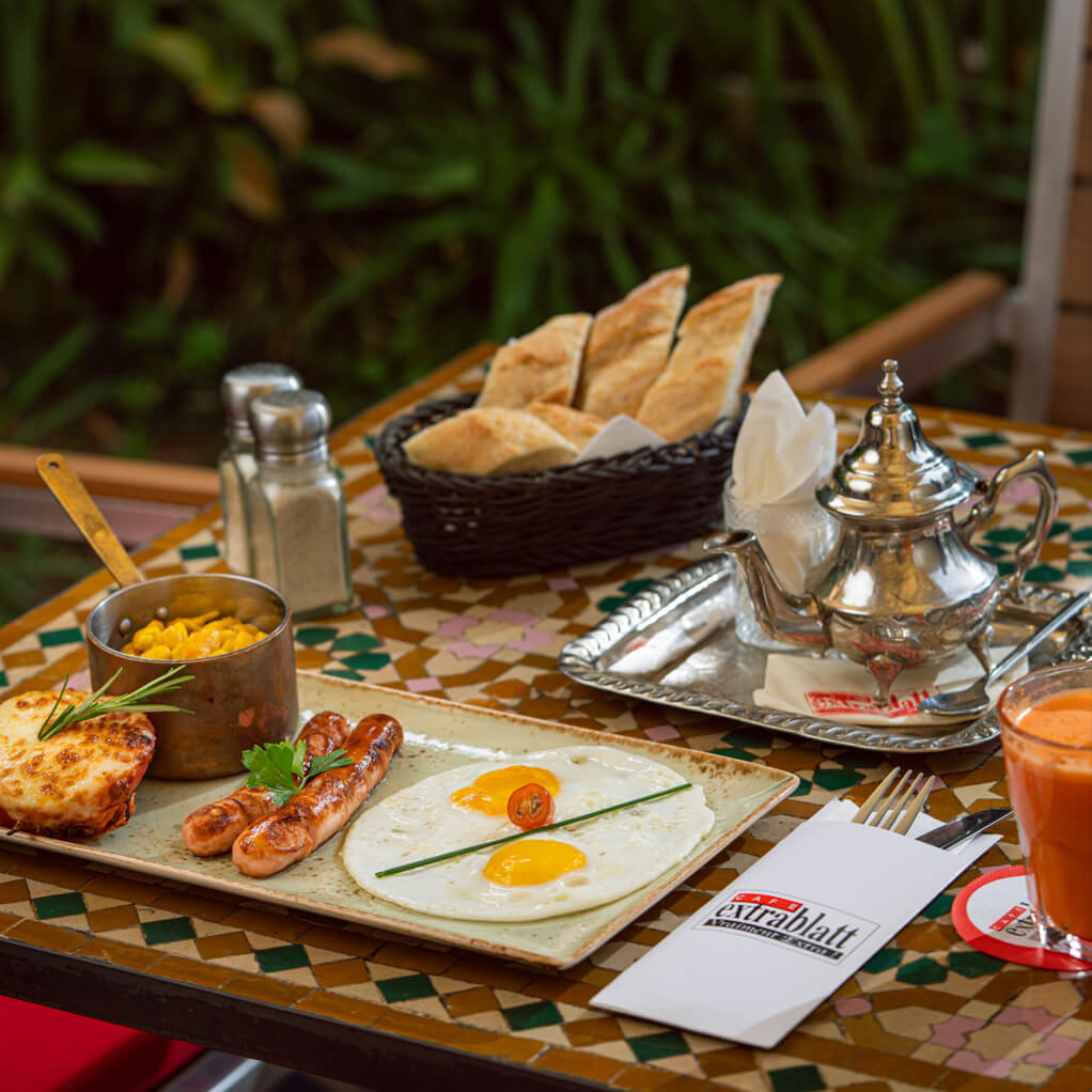 Petit-déjeuner Extrablatt : œufs au plat, saucisses, pain frais et théière sur table zellige
