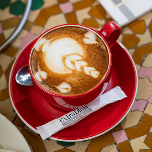 Cappuccino avec latte art dans une tasse rouge Extrablatt, sur table zellige