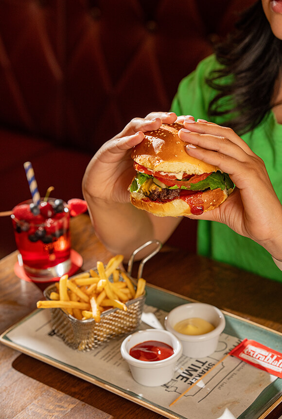 Burger tenu à deux mains, frites maison et cocktail aux fruits rouges